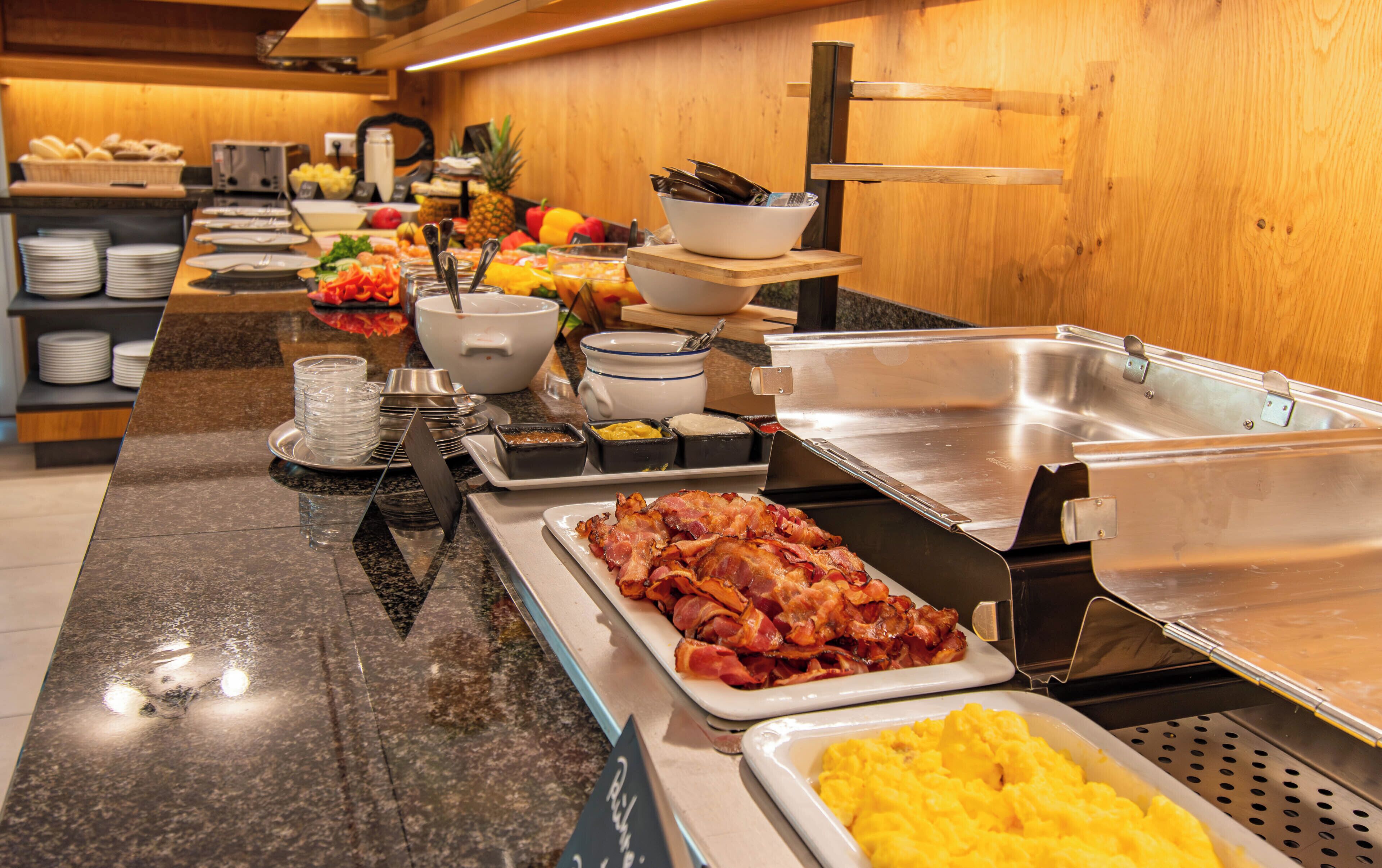 A buffet with various food items including bacon, scrambled eggs, and fruits.