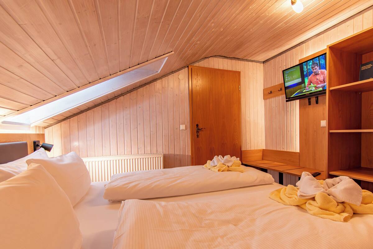 Quarto de cabana de madeira com duas camas, uma televisão e uma prateleira de madeira.