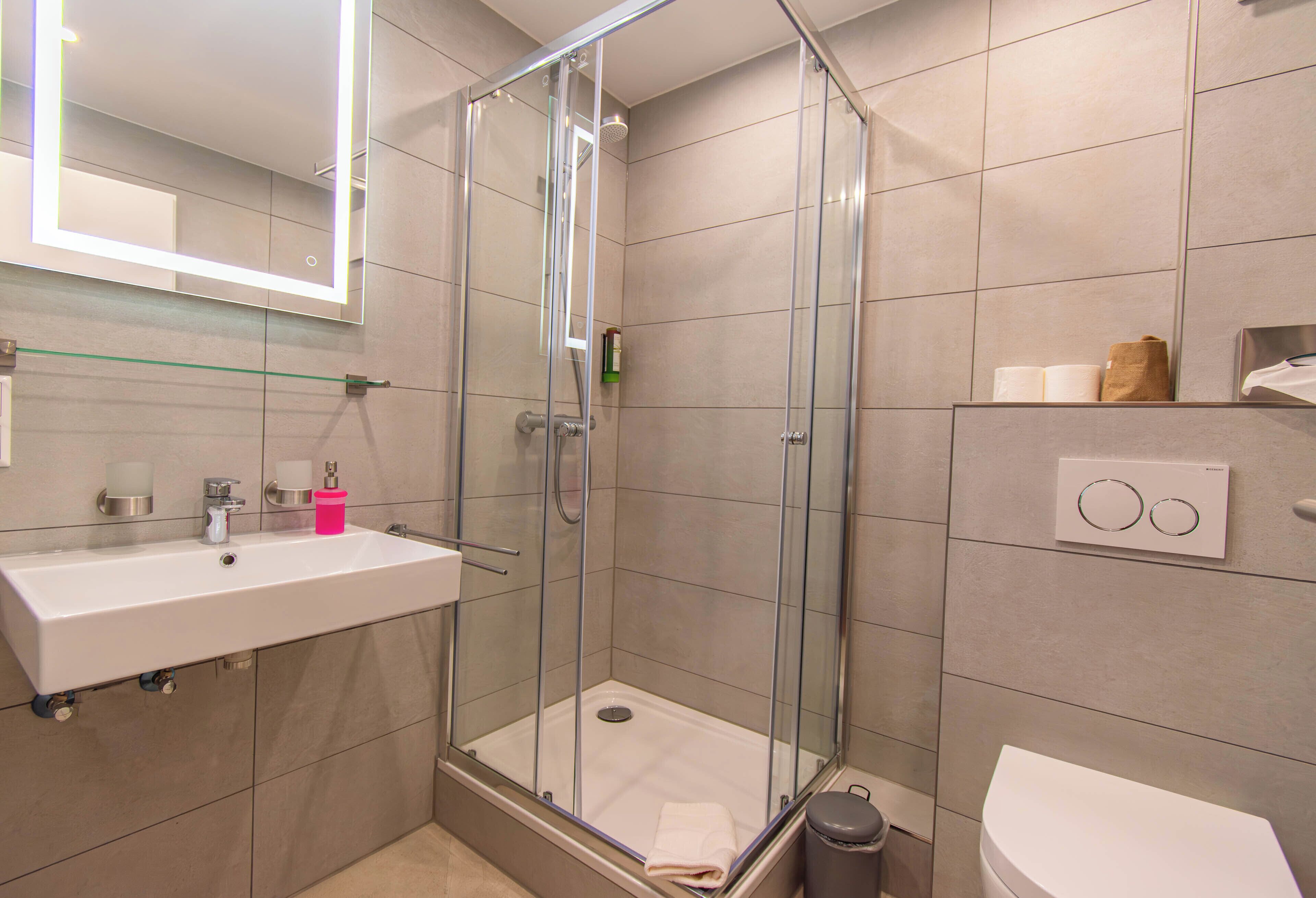 Un baño moderno con ducha de vidrio, lavabo blanco y retrete.