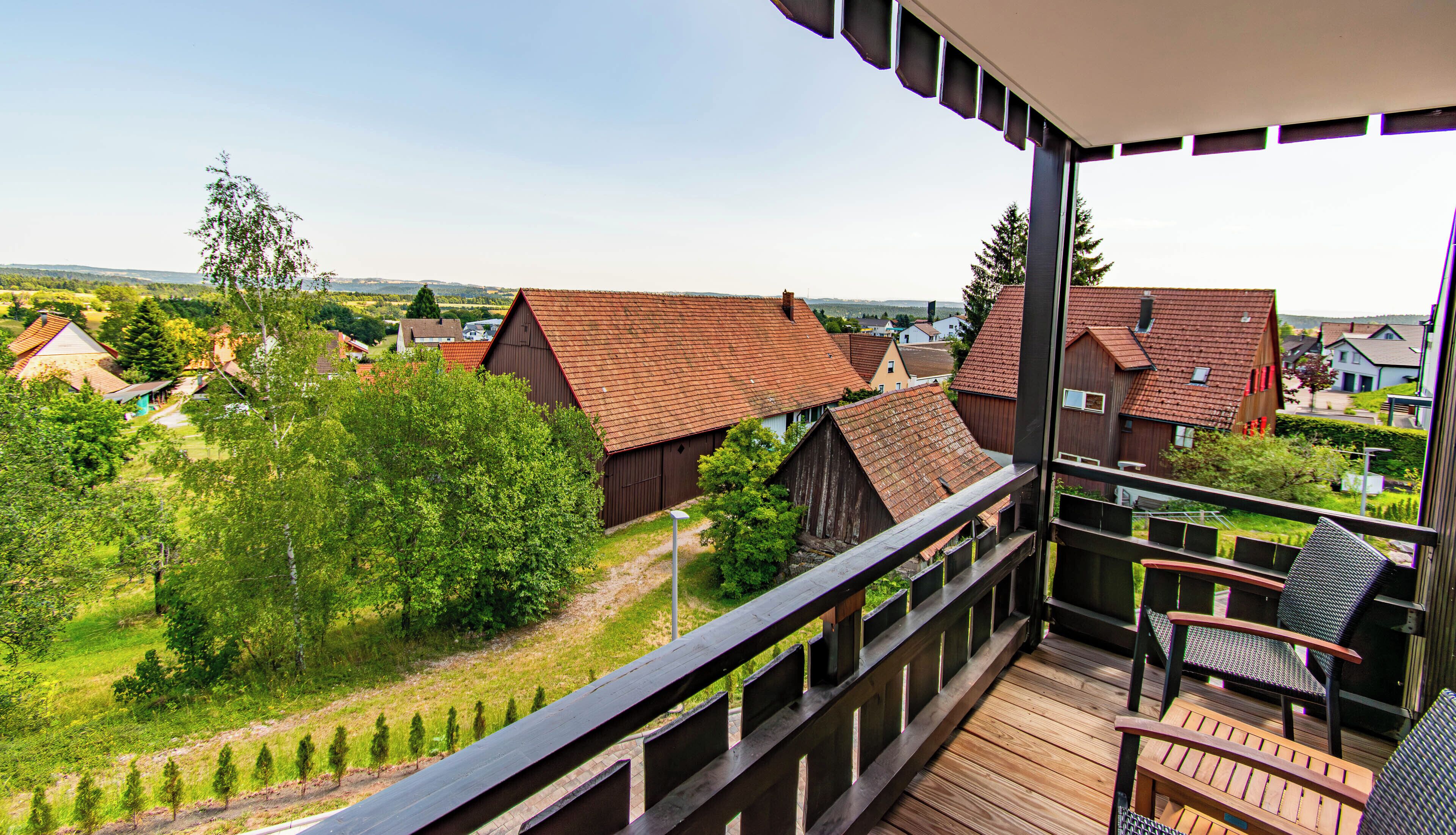 A balcony with a view of a rural village, wooden deck, and outdoor seating.