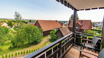 A balcony with a view of a rural village, wooden deck, and outdoor seating.