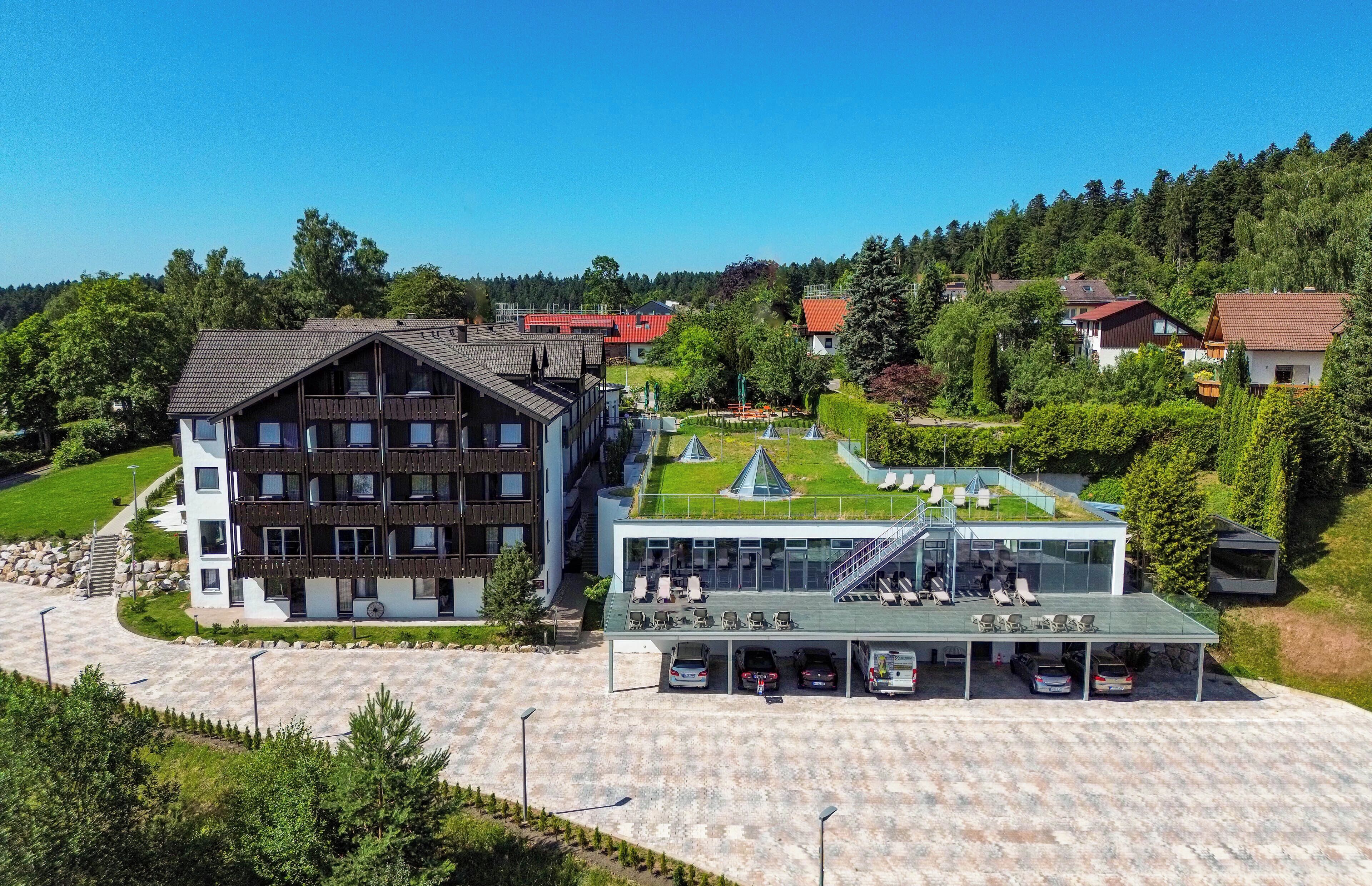 A modern hotel with a large parking area, a swimming pool, and a well-maintained garden.