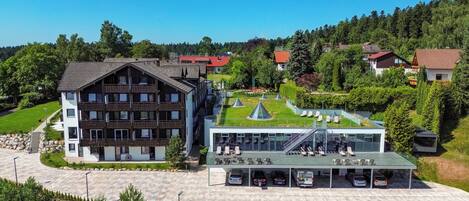A modern hotel with a large parking area, a swimming pool, and a well-maintained garden.