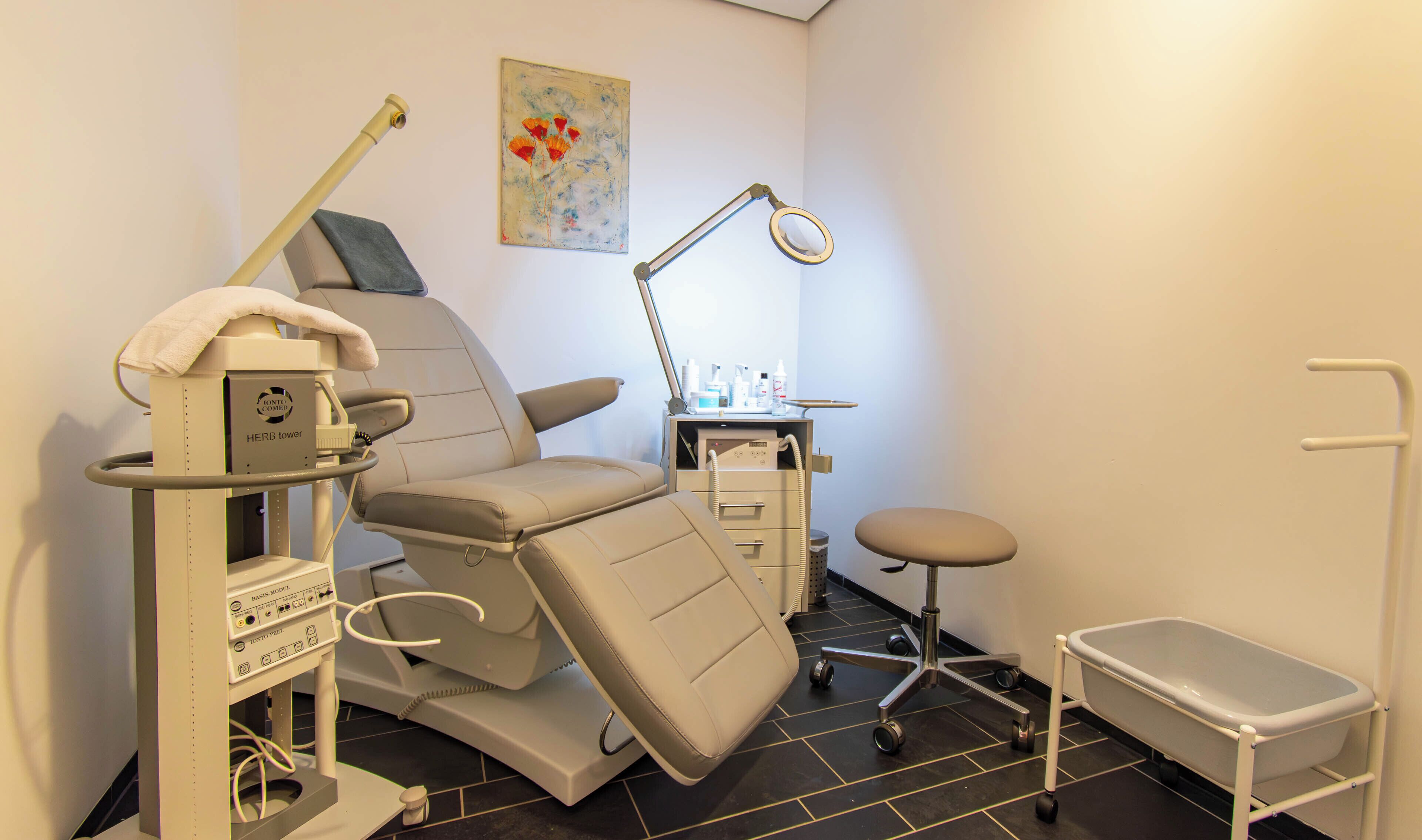 A dental clinic with a reclining chair, a dental light, a sink, and a small stool.