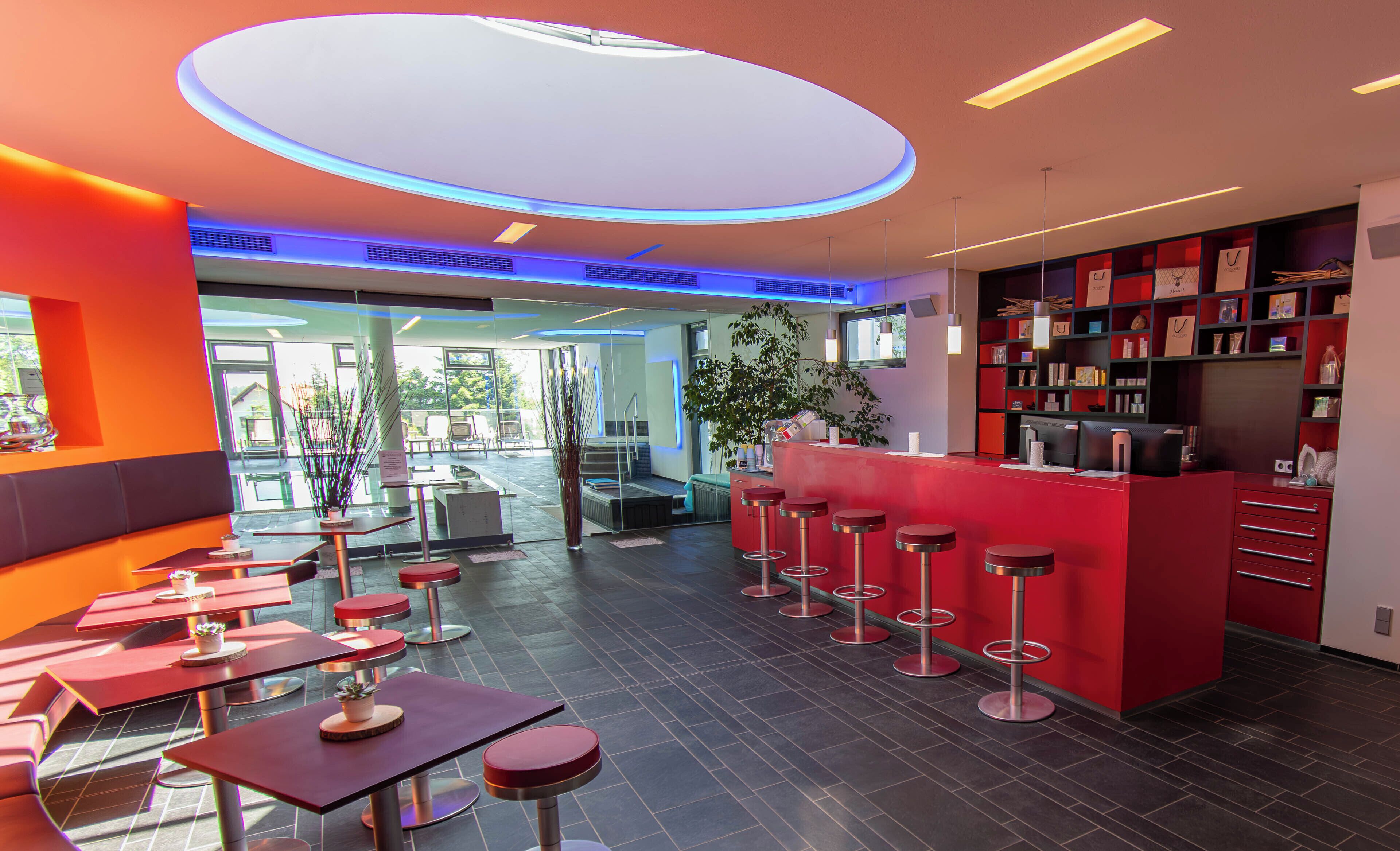 A modern restaurant with red bar stools, a central bar area, and a view of the outdoors.