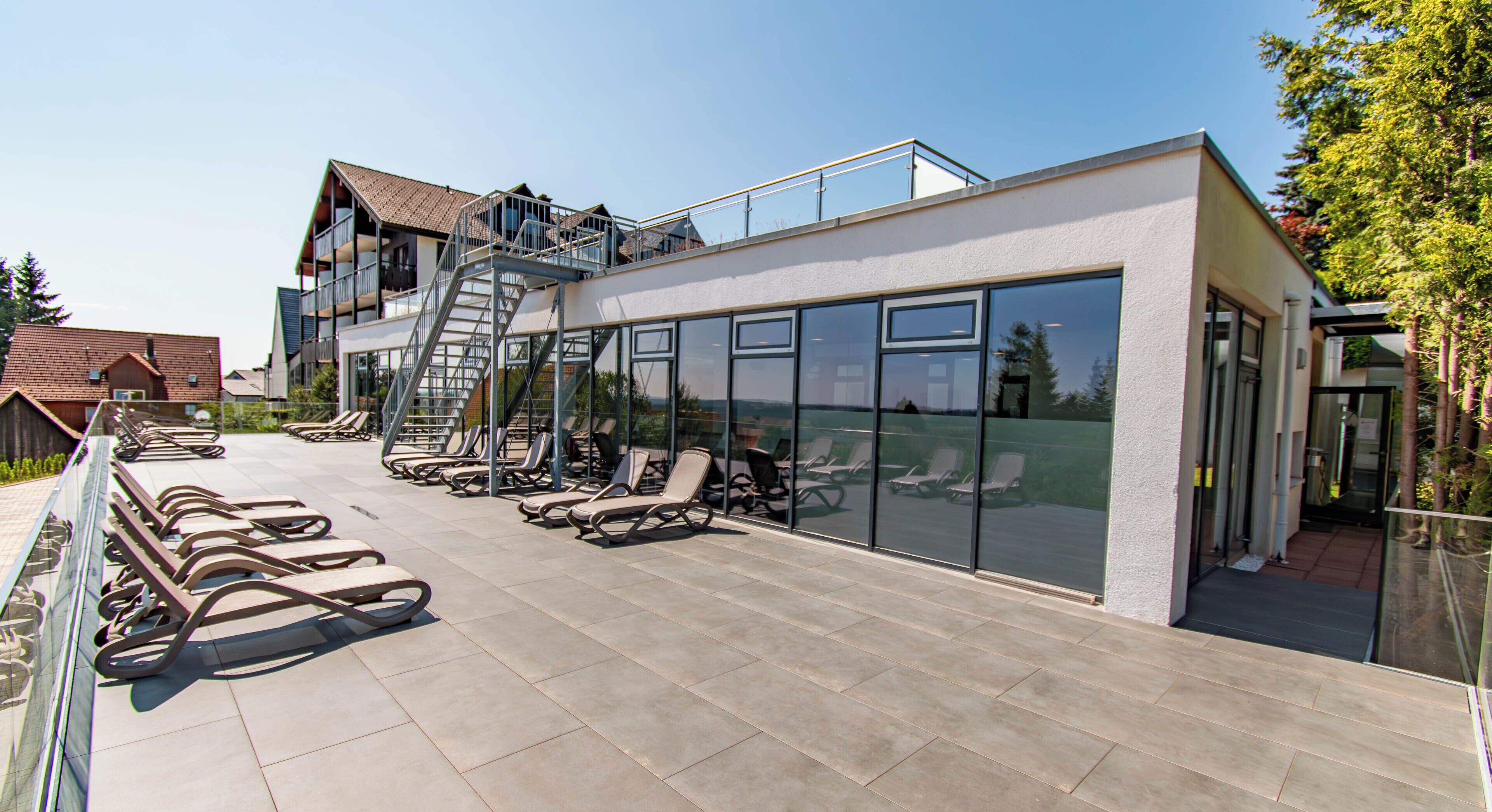 Un bâtiment moderne doté d’une terrasse sur le toit, avec des chaises longues et une façade en verre.