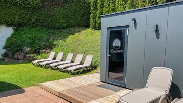 Un espace aménagé au bord de la piscine, avec une terrasse en bois, des chaises longues et un petit bâtiment doté d’une porte.