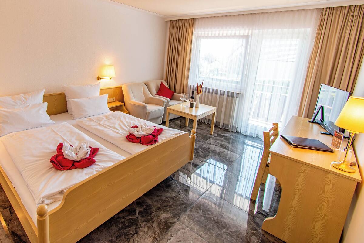 Quarto de hotel com uma cama grande, duas mesas de cabeceira, uma escrivaninha, uma cadeira e uma televisão.