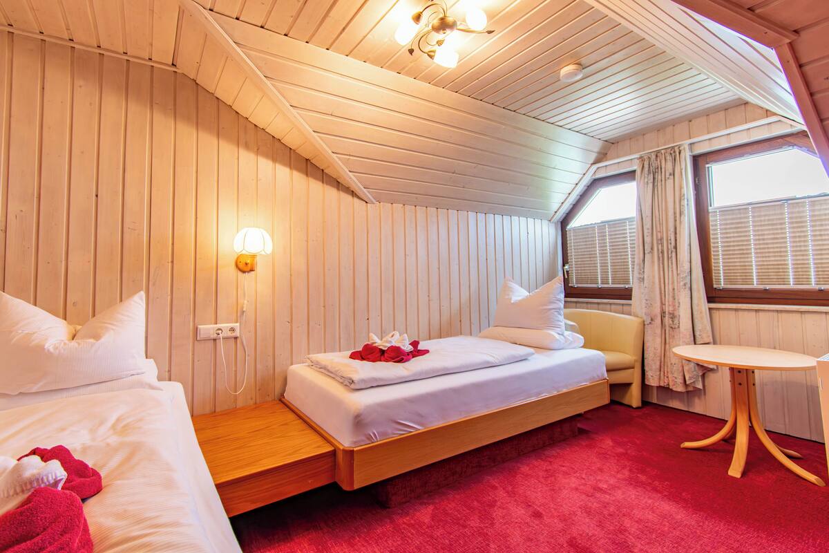Quarto estilo cabana com uma cama, uma mesinha e janela com persianas.
