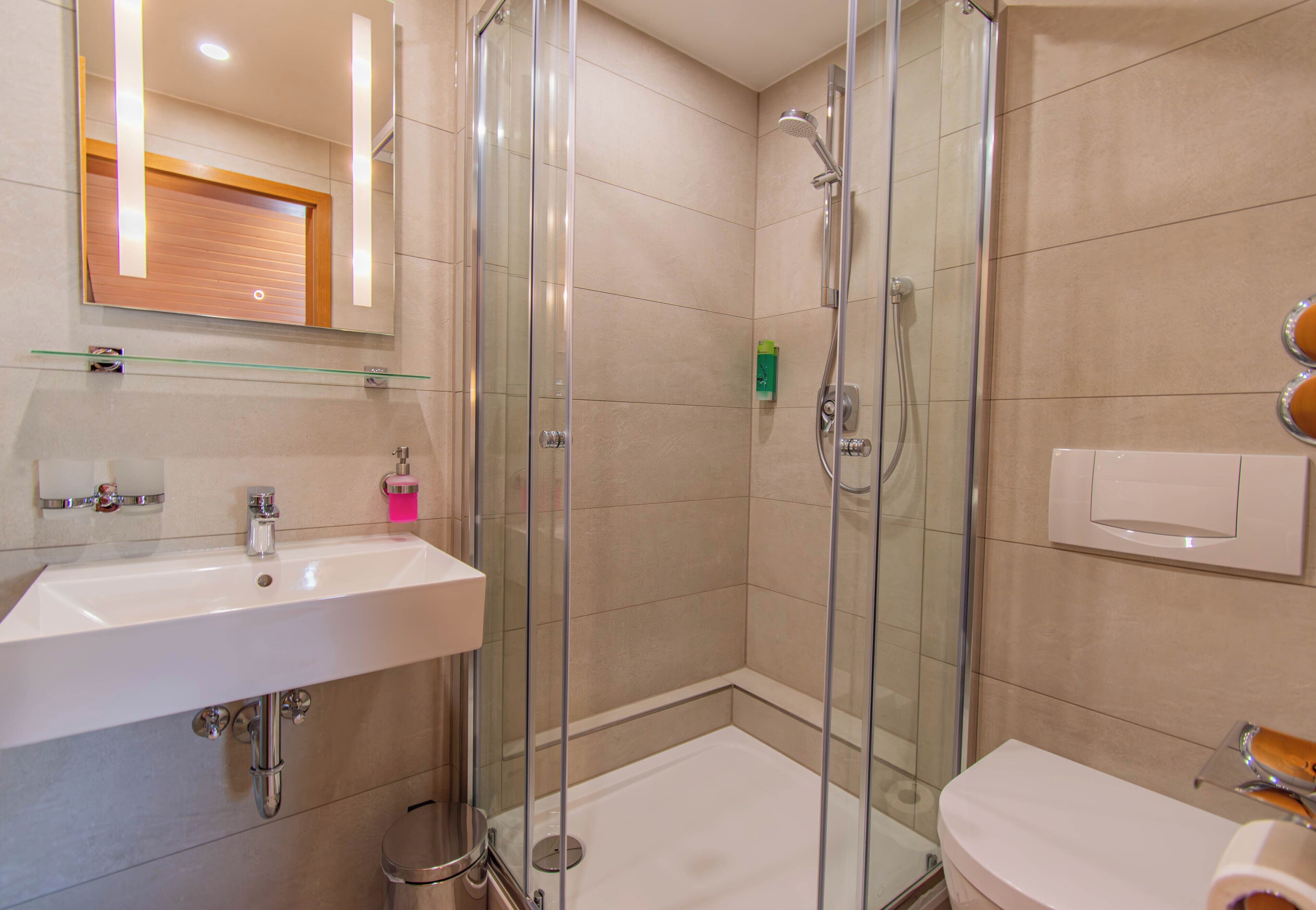 Un baño moderno con cabina de ducha de vidrio, un lavamanos blanco y un inodoro.