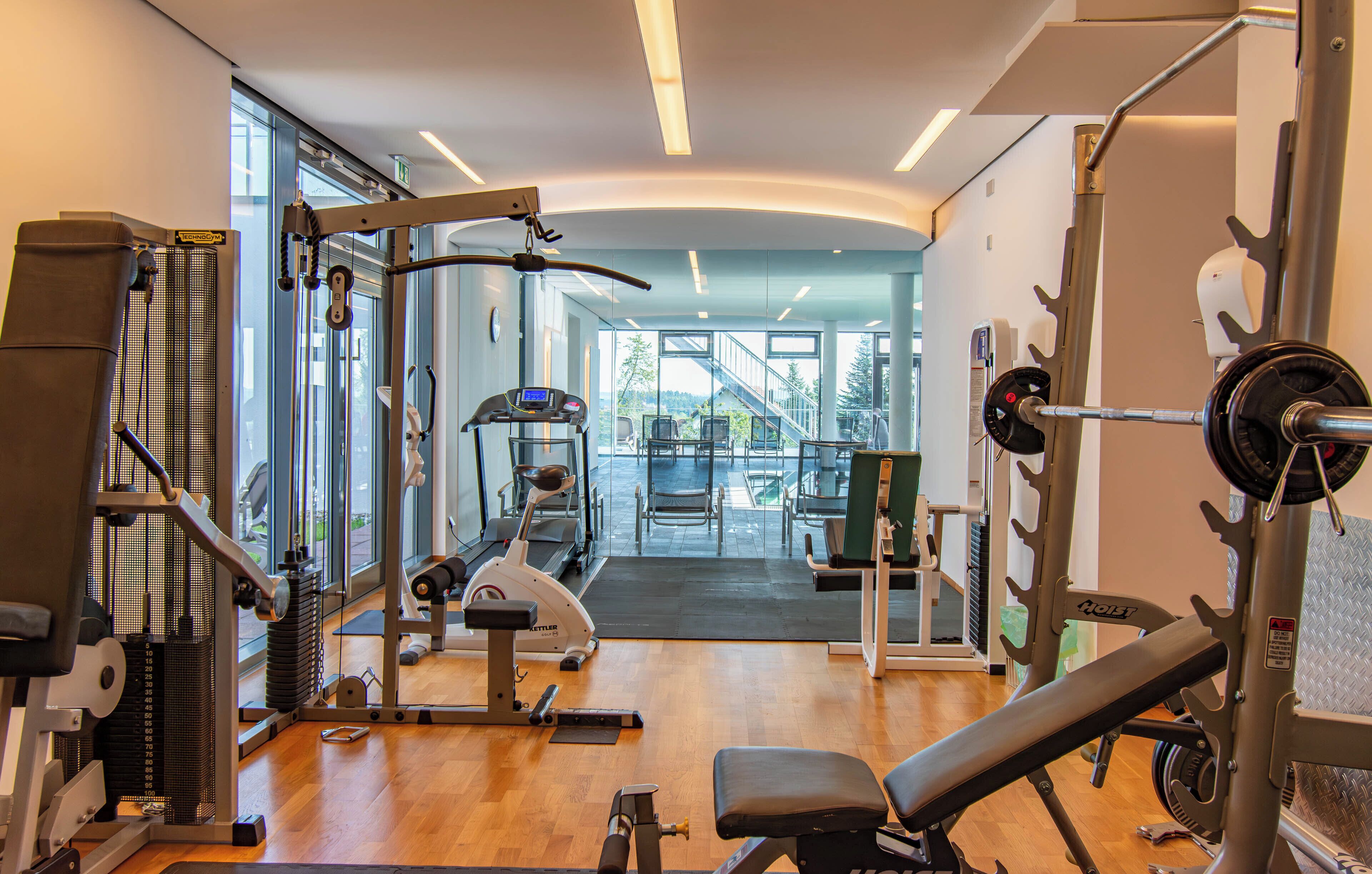 A gym with various exercise equipment, large windows, and a view of a staircase leading outside.