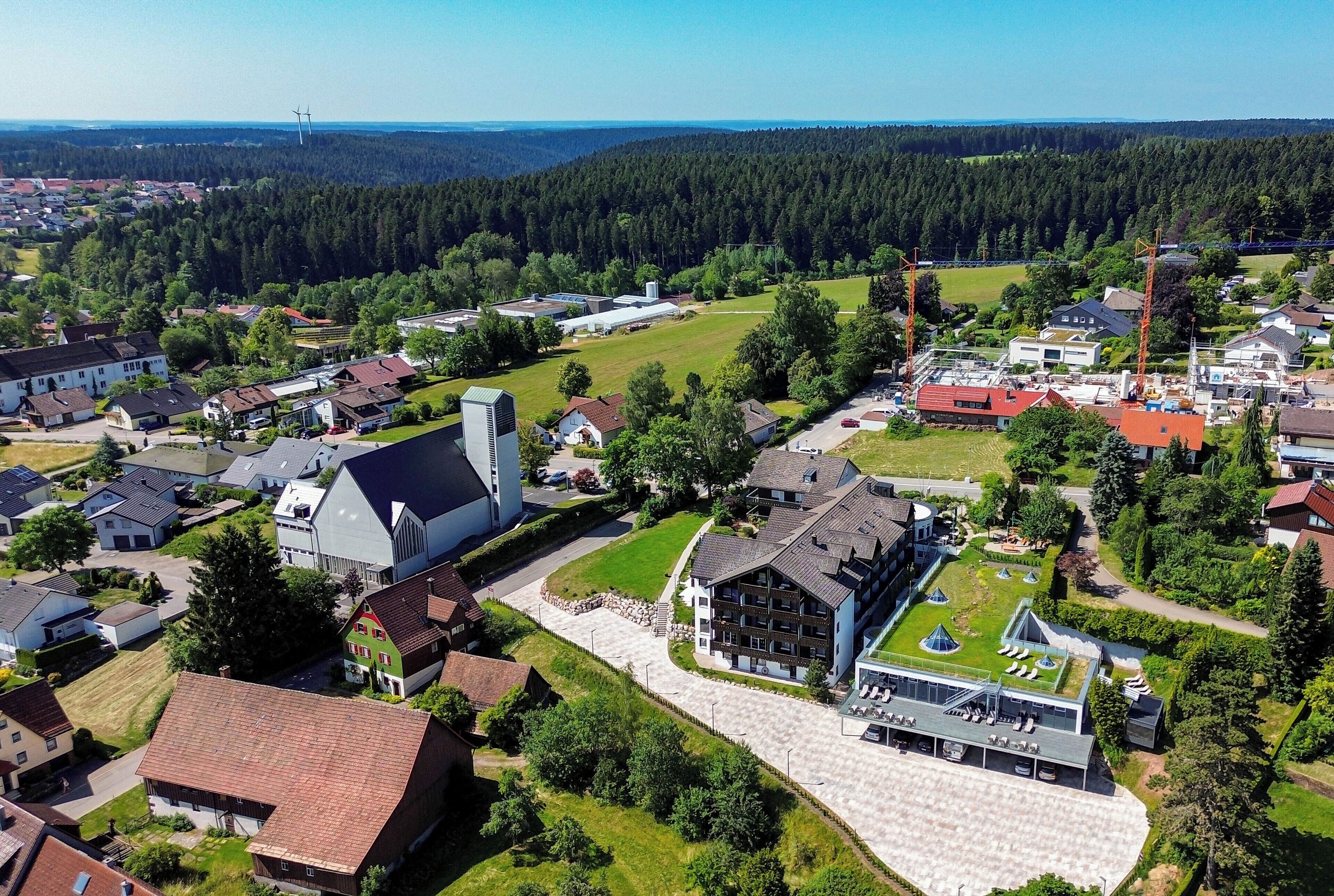 An aerial view of a residential area with houses, a large barn, and a modern building with a green roof.