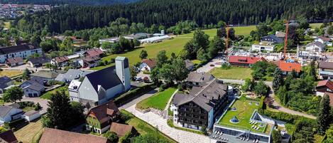 An aerial view of a residential area with houses, a large barn, and a modern building with a green roof.