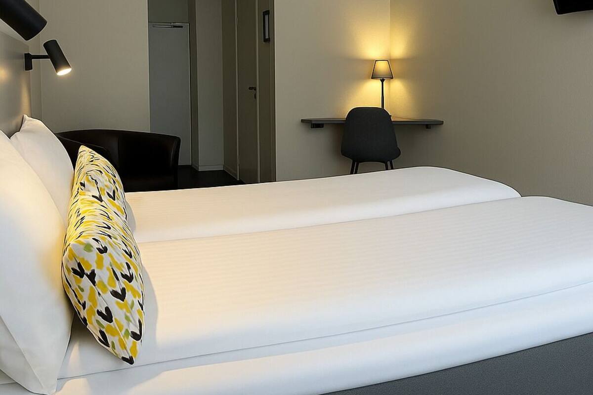 A hotel room with a large bed, a desk with a chair, a TV mounted on the wall, and a door leading to a bathroom.