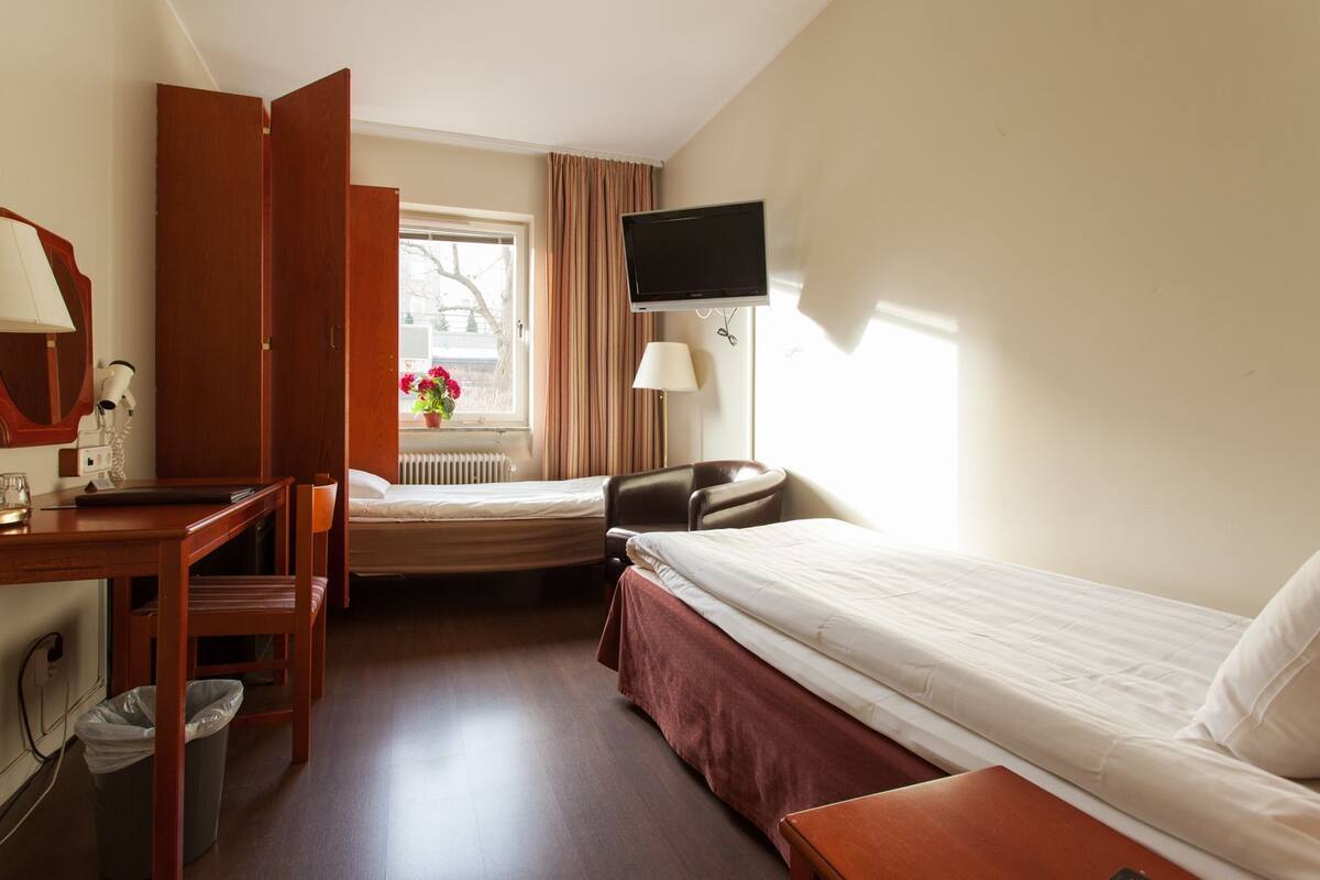A hotel room with a bed, a desk, a chair, a TV, and a window with curtains.
