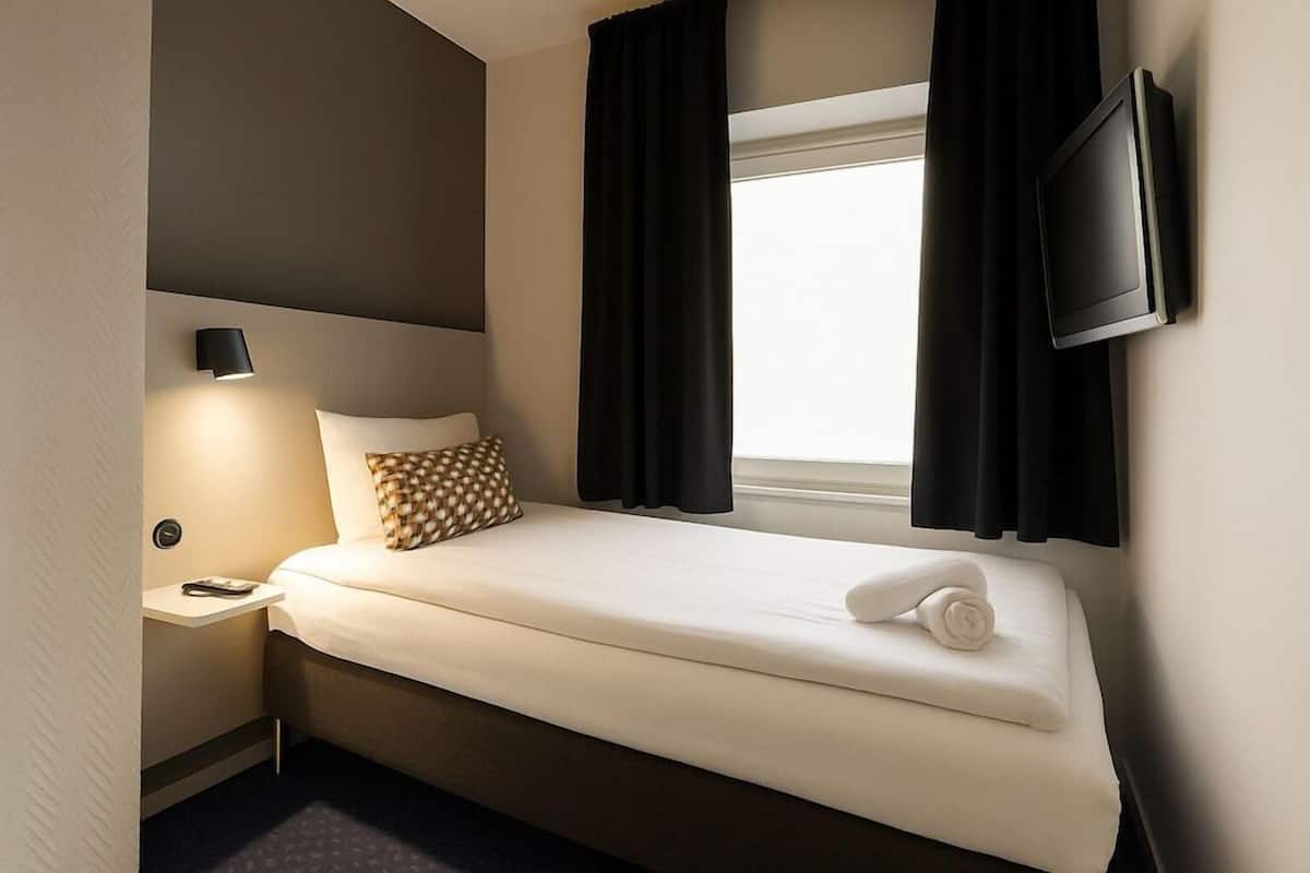 A hotel room with a bed, a nightstand, a wall-mounted TV, and a window with curtains.