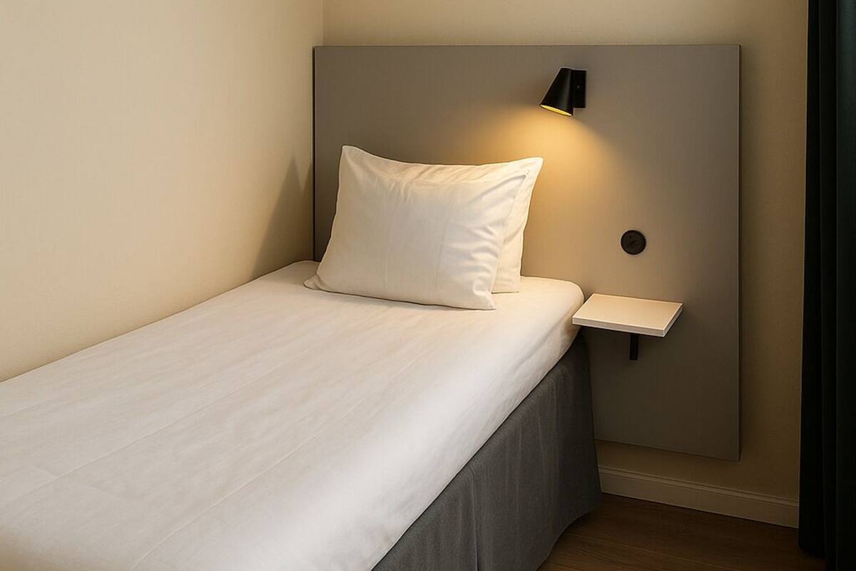 A neatly made bed with a headboard, a bedside table, and a wall-mounted light.