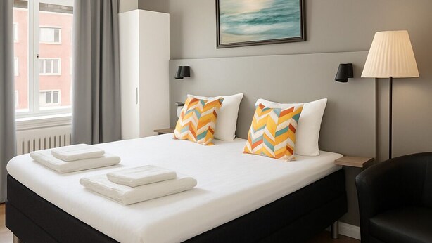 A modern hotel room with a large bed, a desk, and a chair. - Hotell Drott (Norrköping)