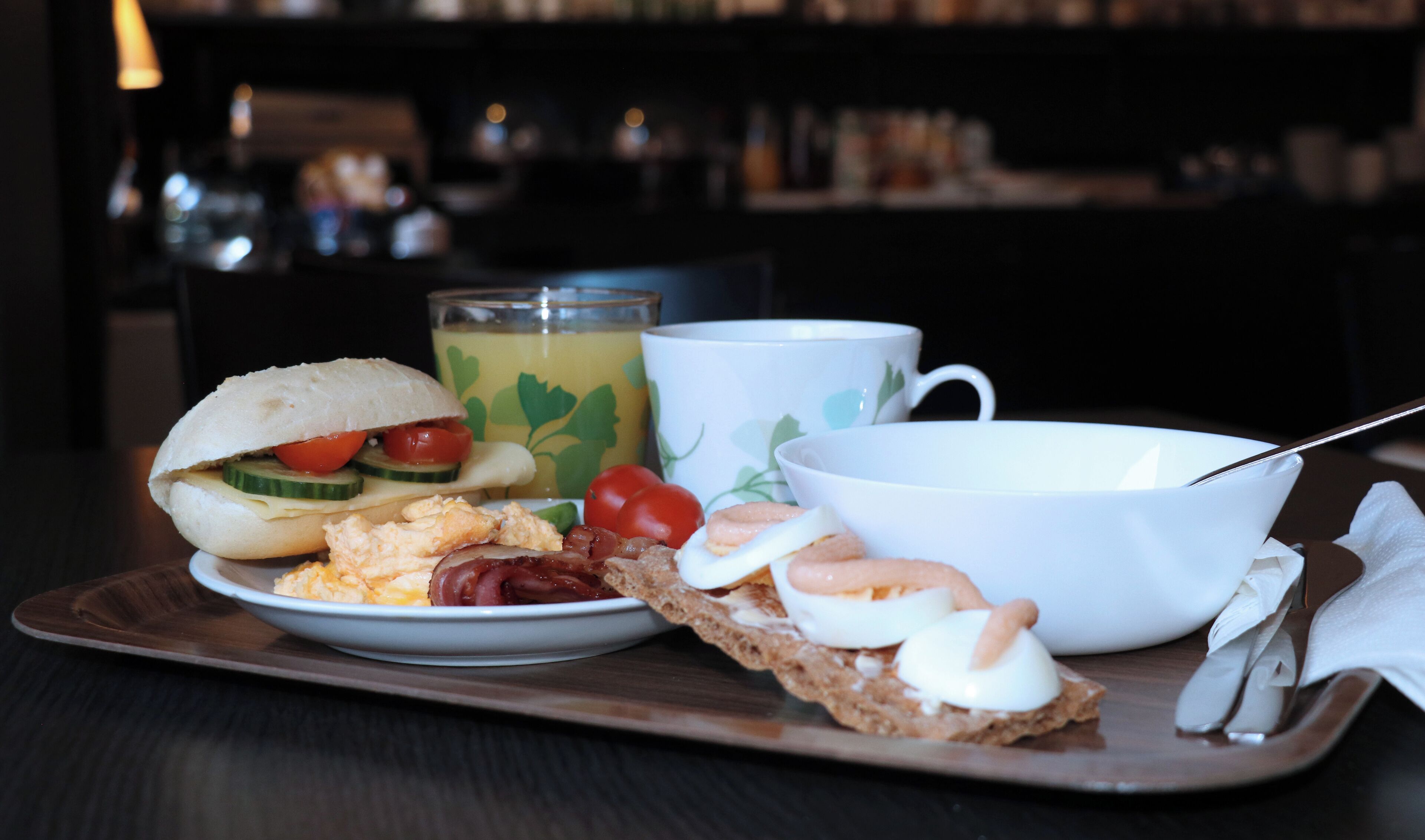 A breakfast tray with a sandwich, eggs, tomatoes, and toast, along with a cup and a glass of juice.