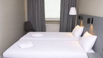 A hotel room with a bed, two pillows, a chair, a lamp, and a bedside table.