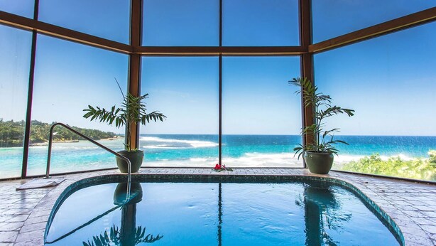 An indoor swimming pool with a view of the ocean through large windows.