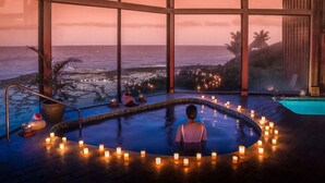 A serene indoor pool area with a view of the ocean at dusk, surrounded by candles.