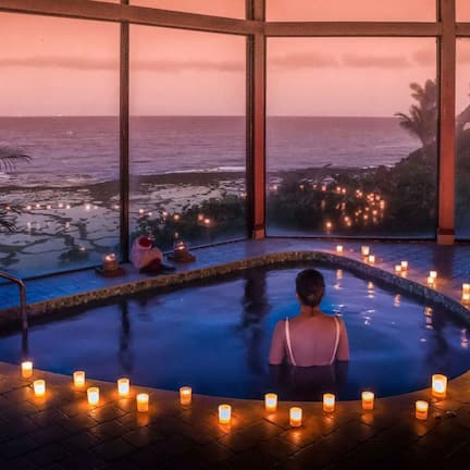 A serene indoor pool area with a view of the ocean at dusk, surrounded by candles.