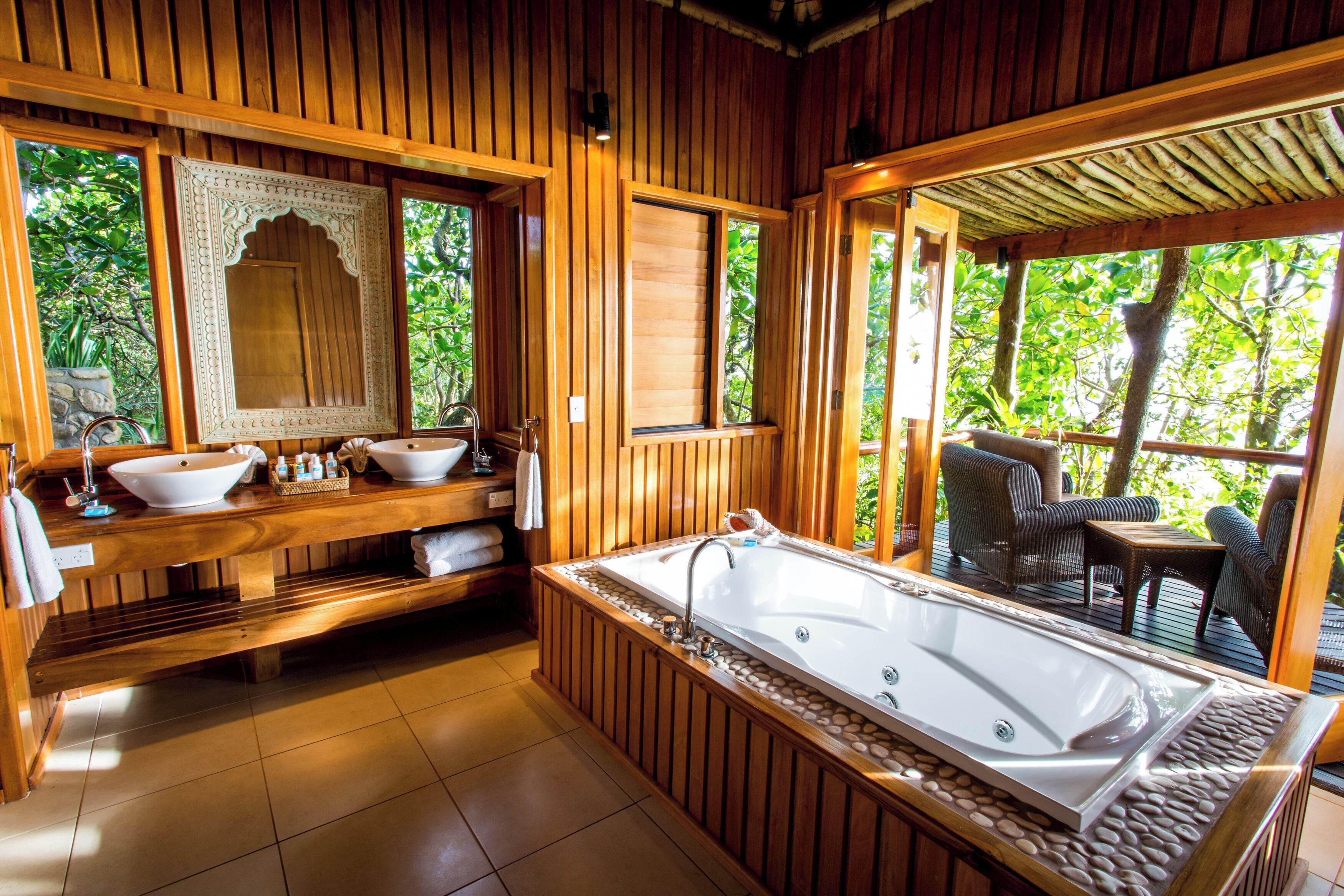 A wooden bathroom with a large bathtub, two sinks, and a mirror.