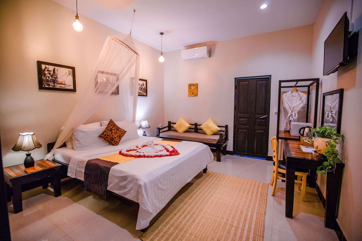 Un dormitorio con cama, mesitas de noche, escritorio, silla, espejo, puerta y lámpara colgante.