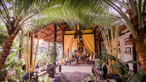 A wooden pathway leading to a covered seating area surrounded by tropical plants and a thatched roof structure. - The Sanctuary Villa Battambang (Battambang)