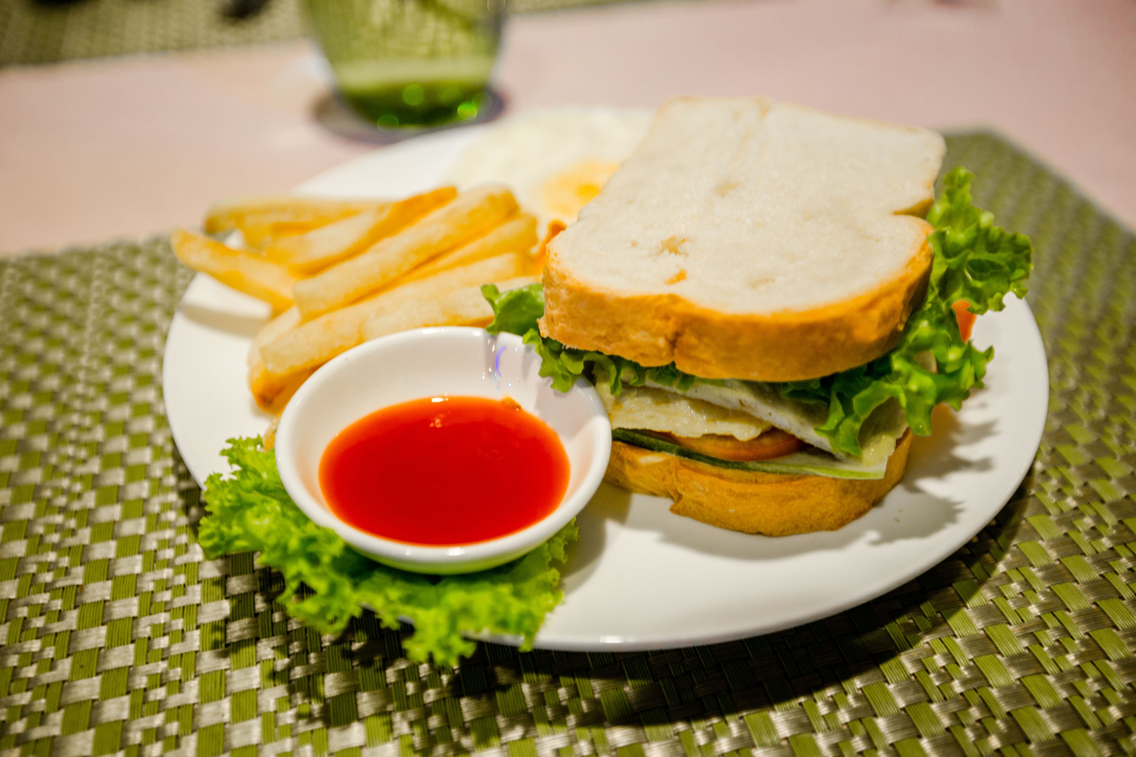 Un sándwich con papas fritas y un recipiente pequeño de salsa en un plato.