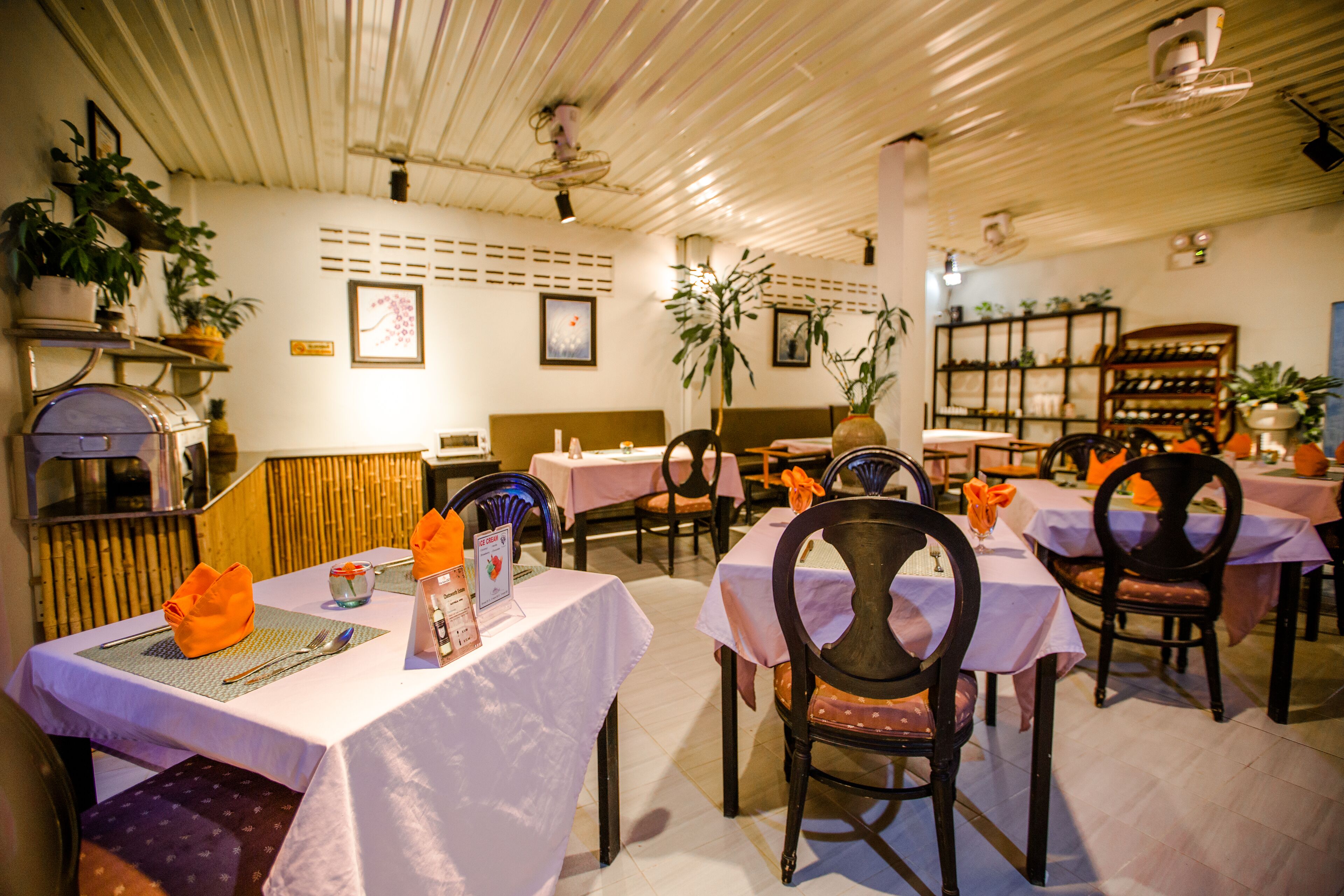 A restaurant with tables set for dining, chairs, and potted plants.