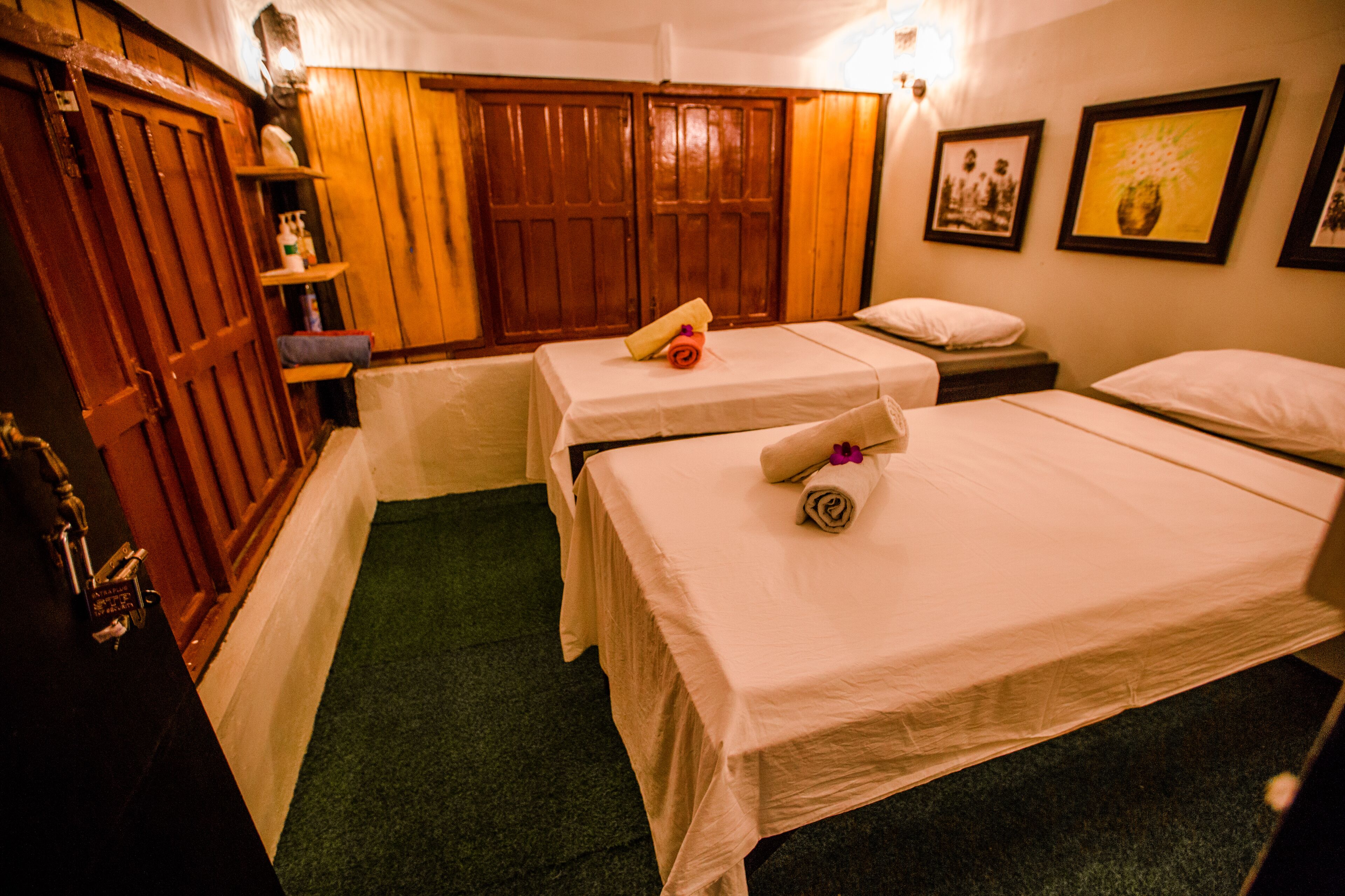 Una habitación de hotel con dos camas individuales, un armario de madera y un pequeño estante con artículos de aseo.
