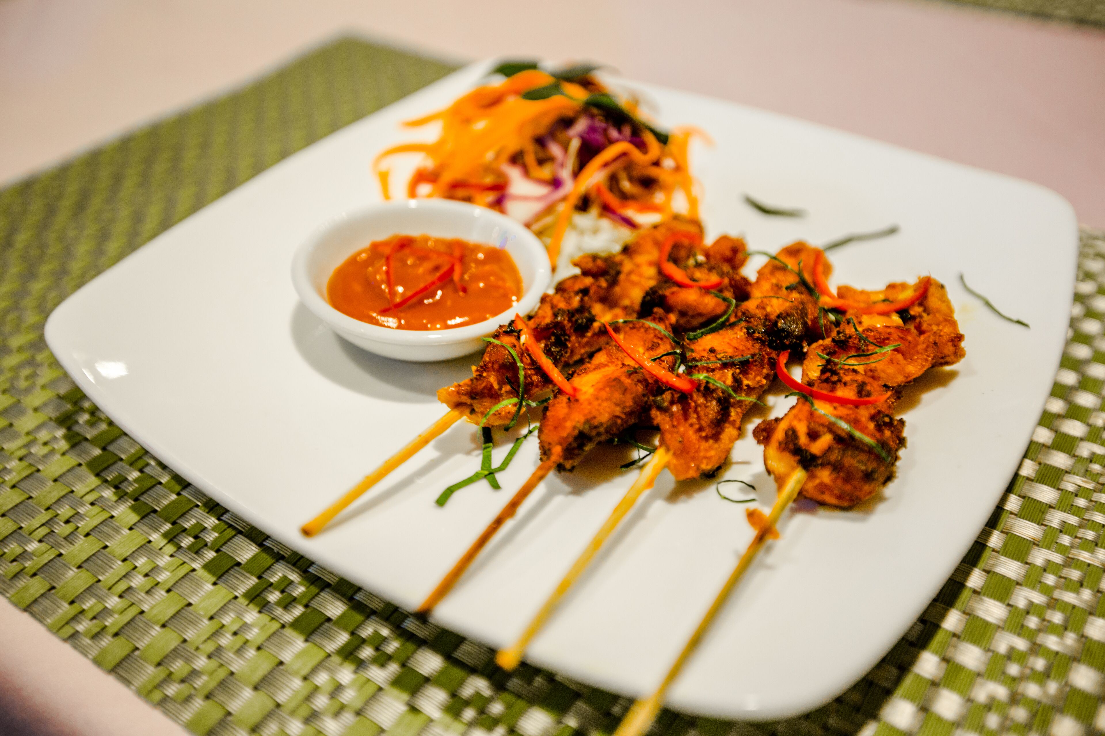 Un plato de brochetas de carne acompañado de arroz y un recipiente pequeño con salsa.