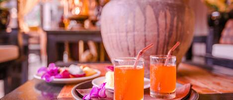 Two glasses of orange beverage on a tray with a plate of food and a decorative vase in the background.