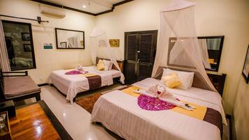 A hotel room with two beds, each with a canopy, a wooden table, and a small seating area.