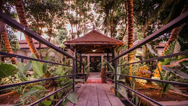 A wooden bridge leading to a gazebo surrounded by tropical plants and trees. - The Sanctuary Villa Battambang (Battambang)