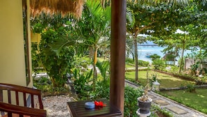 A wooden chair and a small table with a potted plant on a balcony overlooking a lush garden and a body of water.
