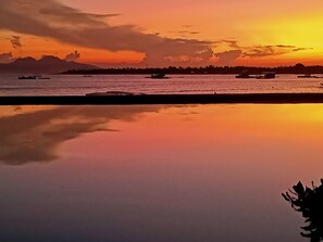 Un paysage paisible au bord de l’eau, au coucher du soleil, avec des bateaux et une côte lointaine.