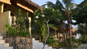 A traditional-style building with a thatched roof, surrounded by lush tropical vegetation including palm trees and flowering plants.