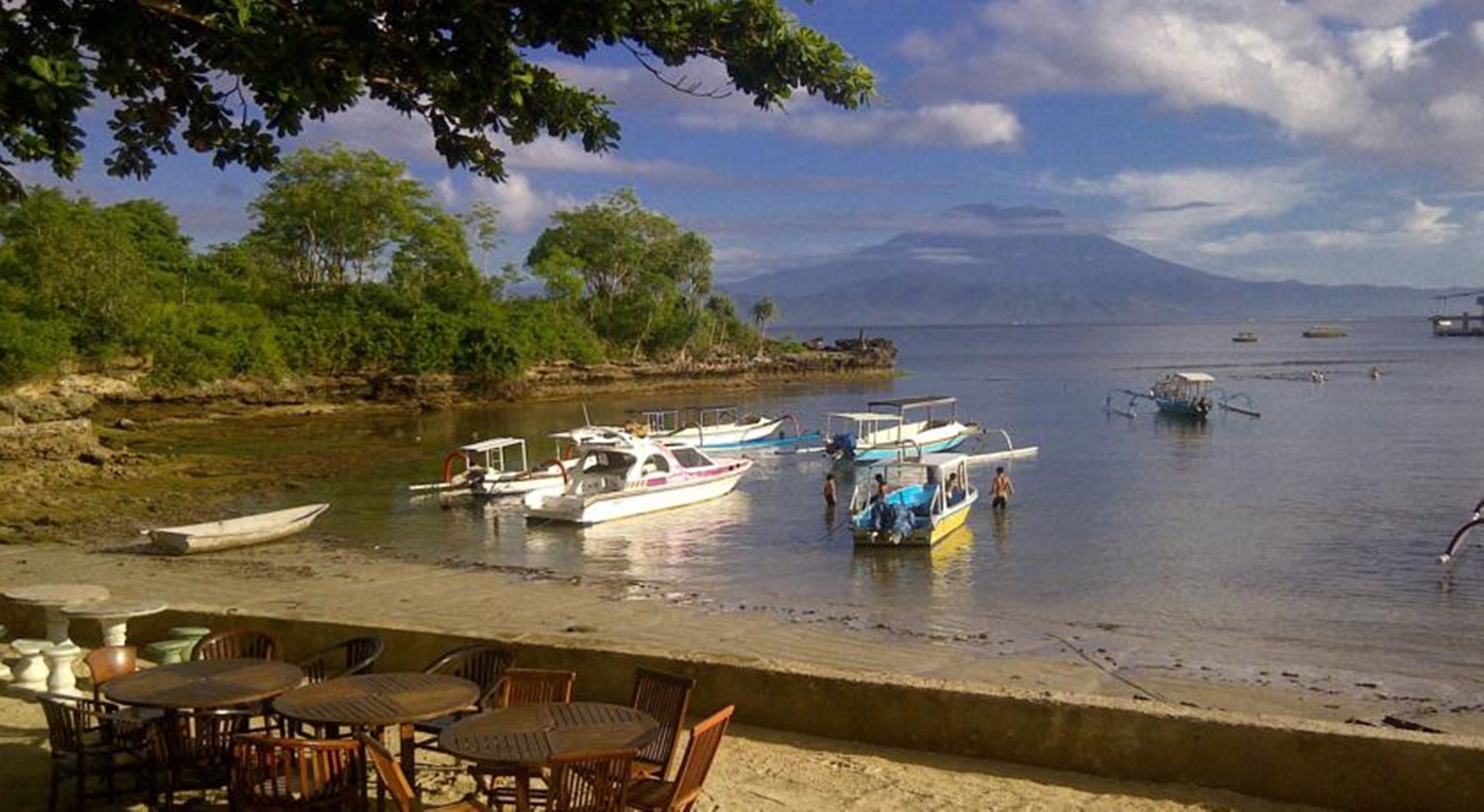Una zona frente al mar con barcos amarrados, una playa de arena y una mesa con sillas.