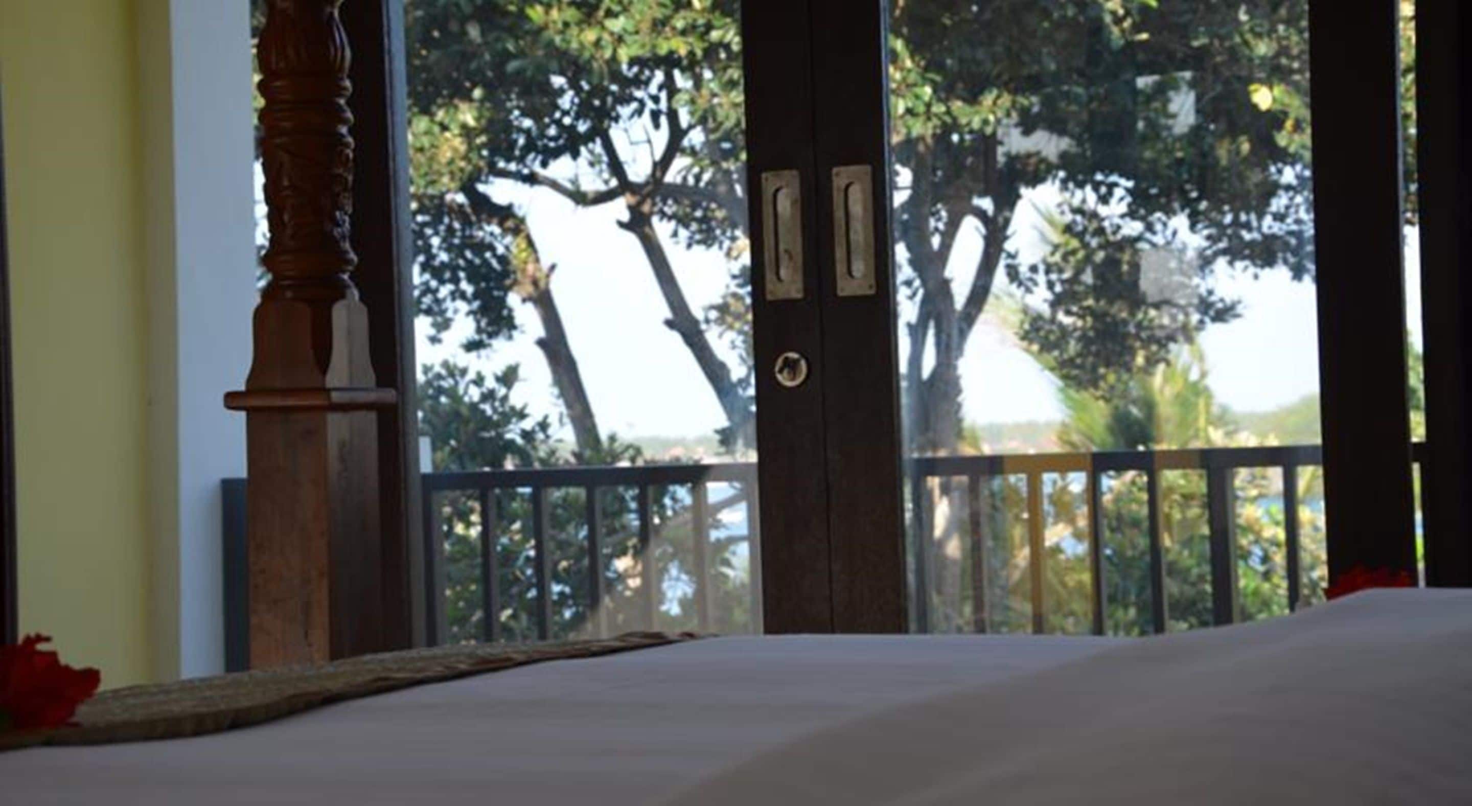 A bedroom with a view of trees through a balcony railing.
