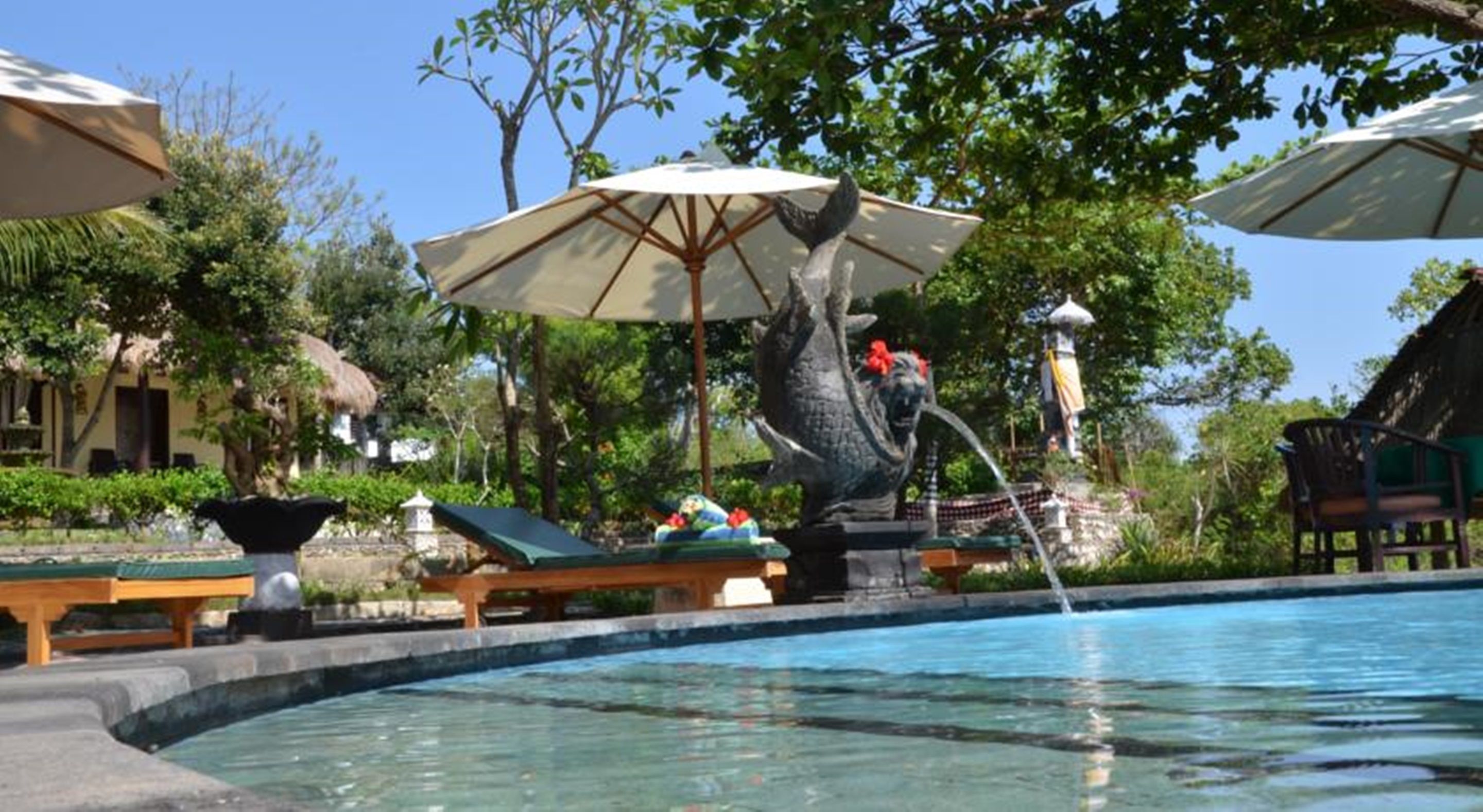 A pool area with lounge chairs, umbrellas, and a statue.