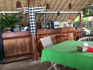 Un restaurant doté d’un toit de chaume, de meubles en bois et d’une nappe verte.