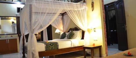 A four-poster canopy bed with a nightstand and a lamp, a wooden bench, and a mirror in a hotel room.