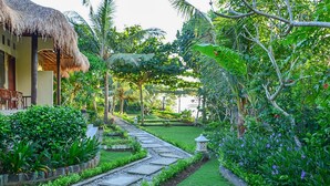 A tropical garden with a stone pathway leading to a thatched-roof building.