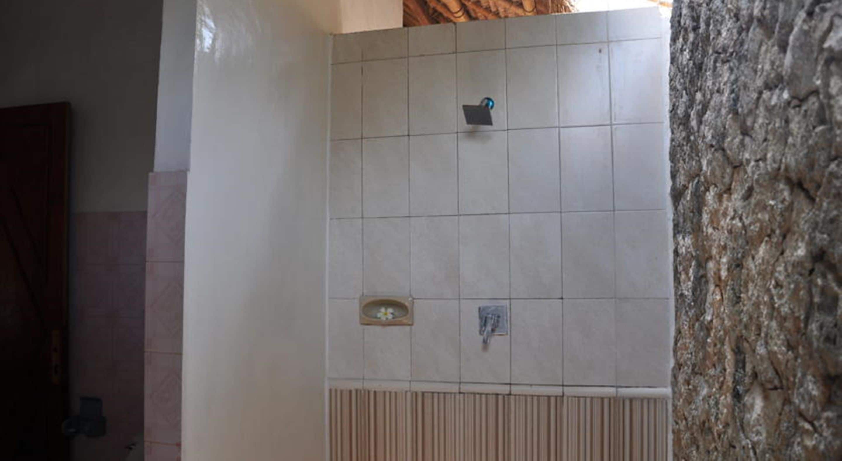 A tiled shower area with a hand dryer and a small shelf.