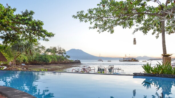 An infinity pool with a view of boats and a mountain in the background.