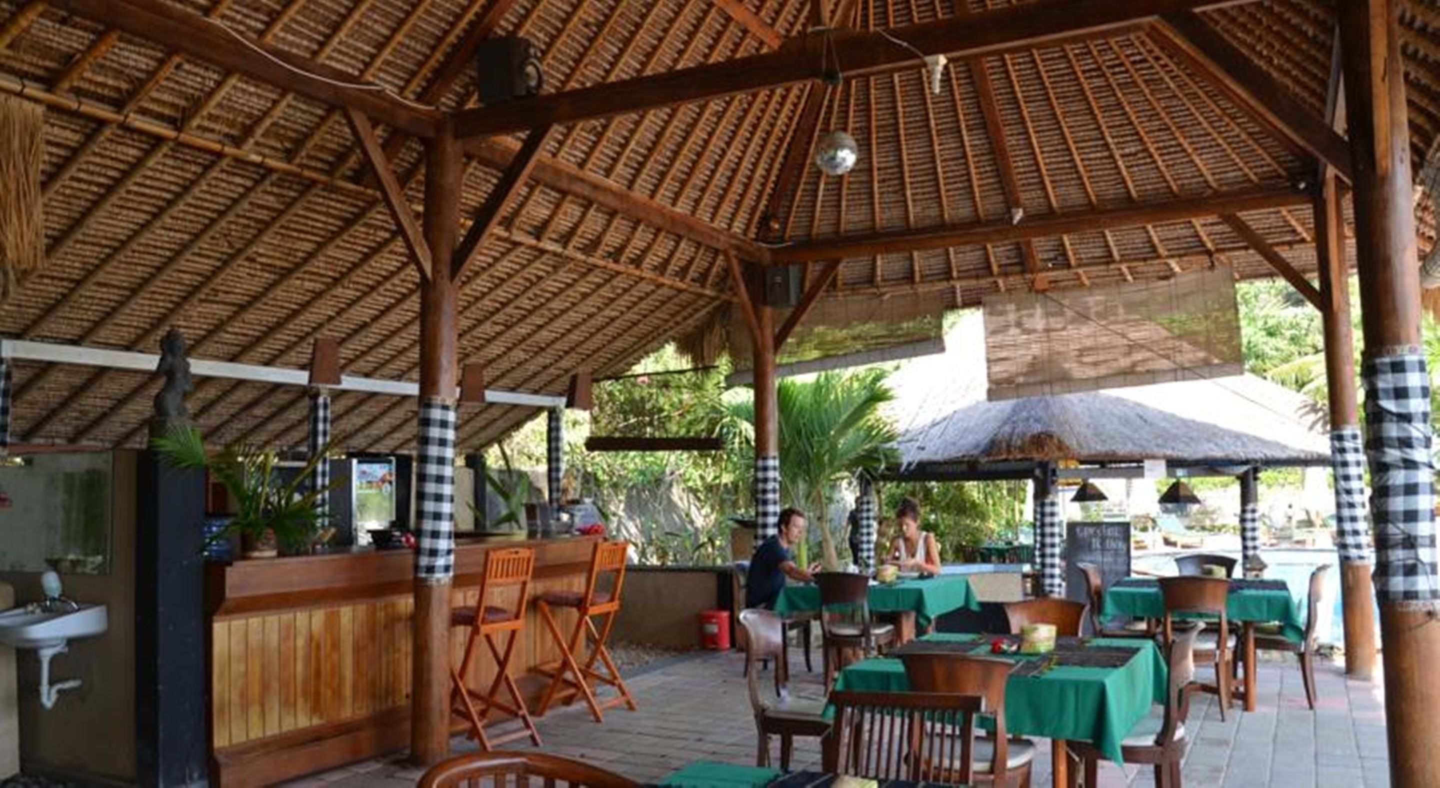 Un restaurante al aire libre con techo de paja, mesas y sillas de madera.