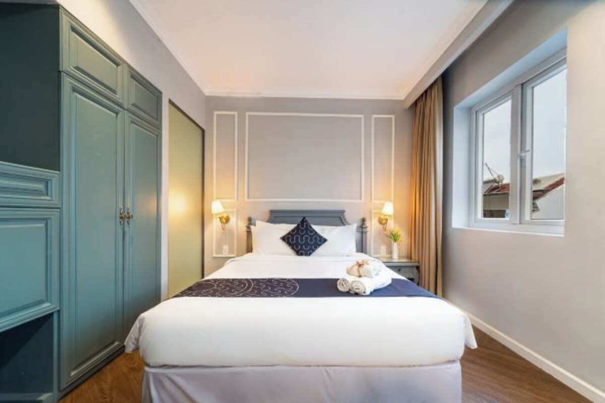 Habitación de hotel con una cama grande, dos lámparas de noche, una ventana con cortinas y un armario.